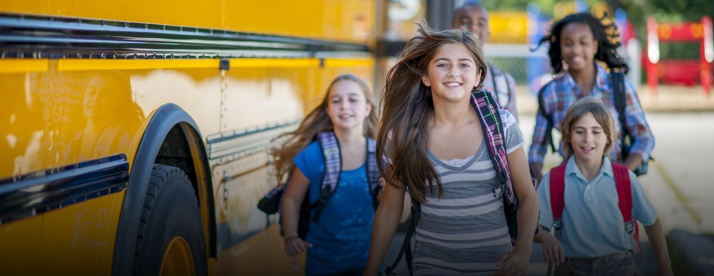 Group of smiling children running off of a school bus