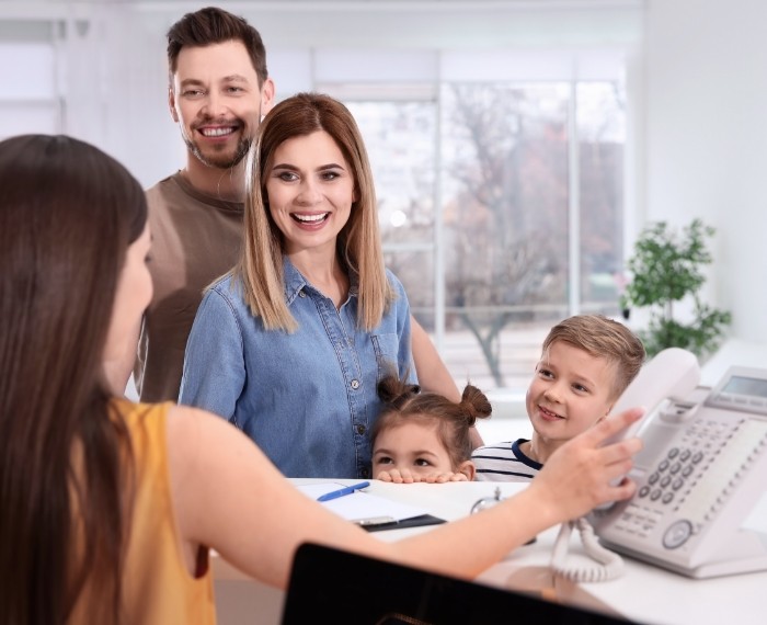 Family of four smiling at dental office receptionist