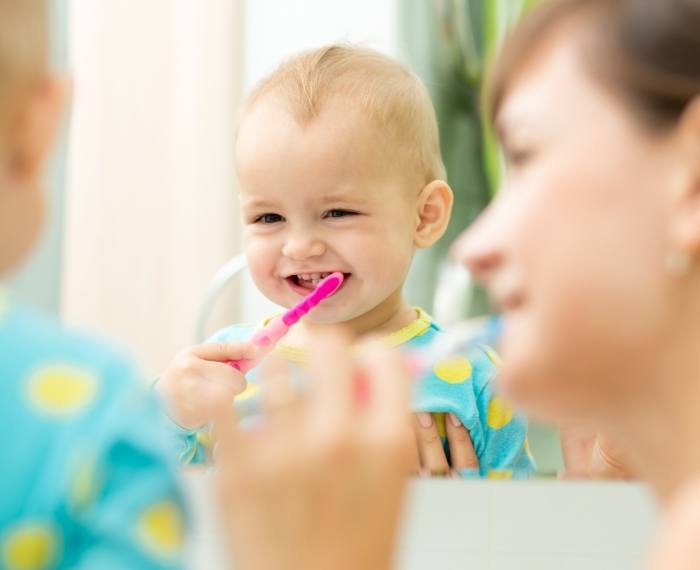 Mother showing her toddler how to brush their teeth