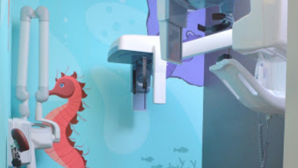 Dental X ray machine in front of seahorse painting on wall