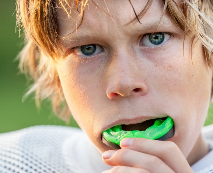 Young boy placing green athletic mouthguard into his mouth