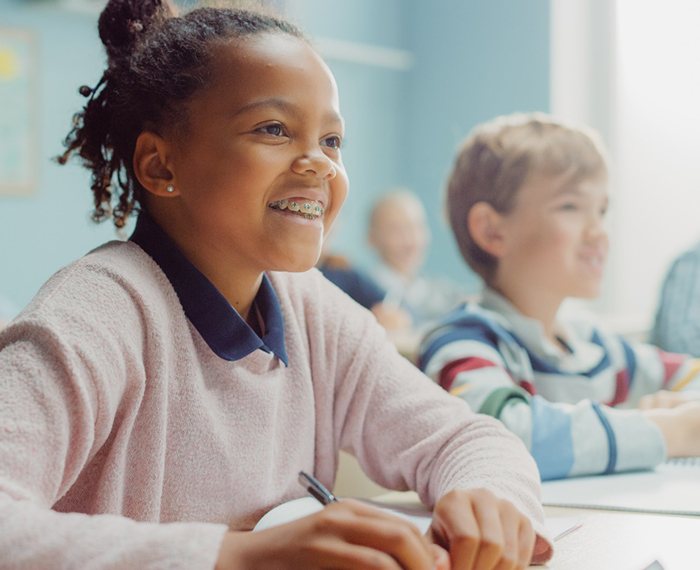 Child with traditional braces smiling in classroom