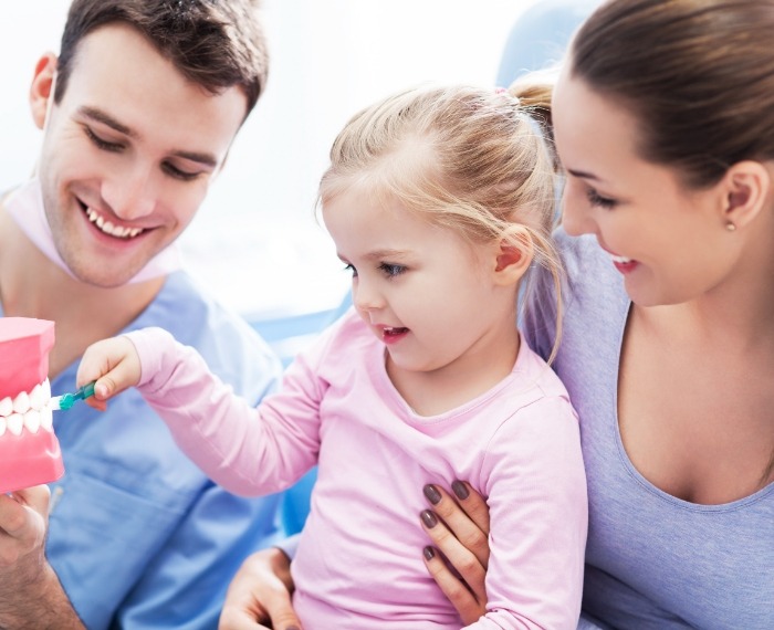 Young girl in dental office brushing a model of the teeth