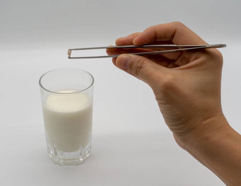 Person holding tooth with tweezers next to glass of milk